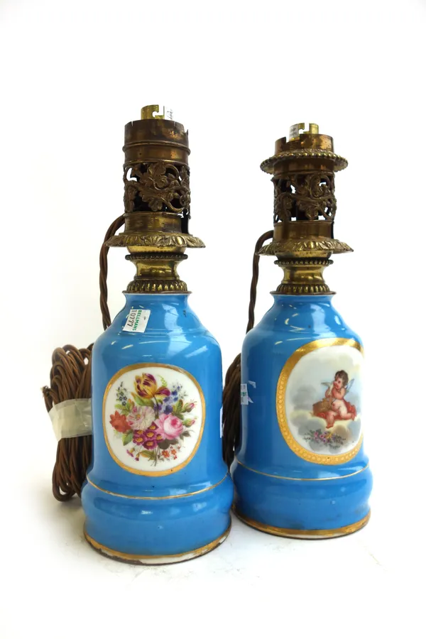 A pair of porcelain oil lamp bases (converted), each decorated with Cupid figures and still life flowers against a gilt and blue ground, 30cm high, (2