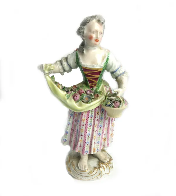 A Meissen figure of a girl, early 19th century, standing with an apron full of flowers and holding a basket of flowers in her left hand, blue crossed