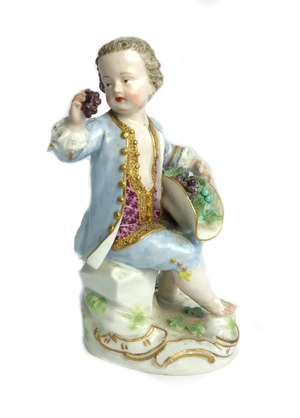 A Meissen figure of a youth, circa 1770, the boy seated on rocky mound, holding a bunch of grapes in his right hand and with a hat full of grapes on h
