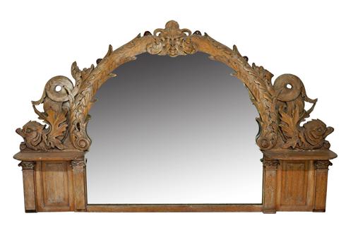 A 19th century carved limed oak arch top mirror, centred with a green man mask flanked by sea serpents, 244cm wide x 152cm high.  Illustrated