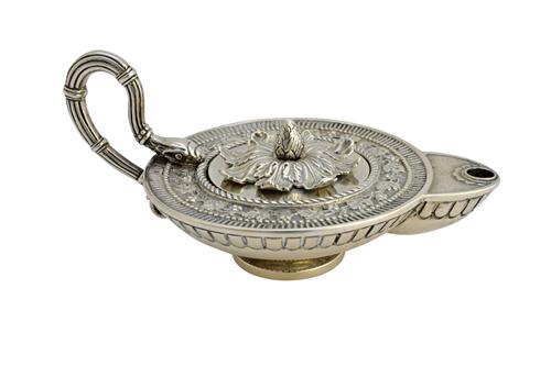 A silver table lighter, modelled as a classical style oil lamp, decorated with a border of fruiting vine and with a serpentine handle, London 1910, we