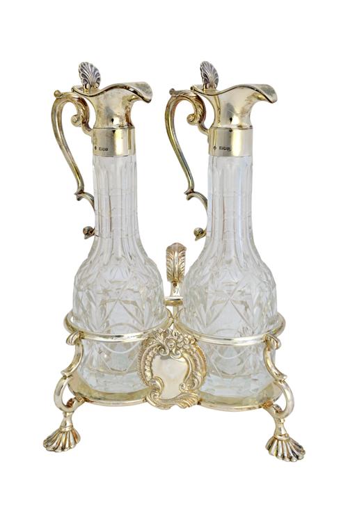 A silver twin bottle oil and vinegar cruet stand, in a mid 18th century inspired design, fitted with a rococo style cartouche and raised on four scall
