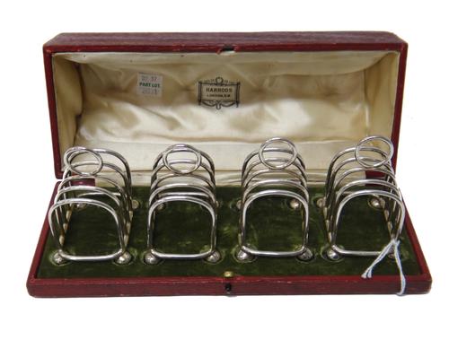 A set of four plated small five bar toastracks, each having a loop shaped handle and raised on four spherical feet, with a Harrods fitted case and a s