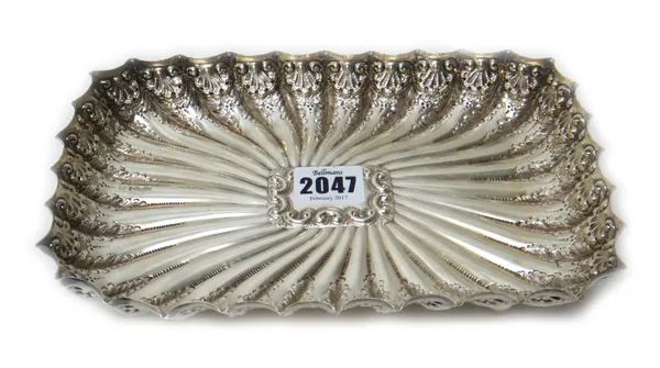 A late Victorian silver shaped rectangular dish, having curved fluted decoration, within embossed sides, raised on four spherical feet, Sheffield 1900