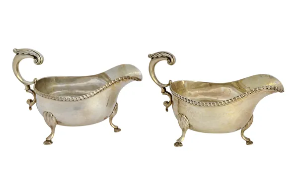 A pair of silver sauceboats, each with a scrolling handle, gadrooned rim and raised on three shell capped feet, London 1910, combined weight 643 gms.