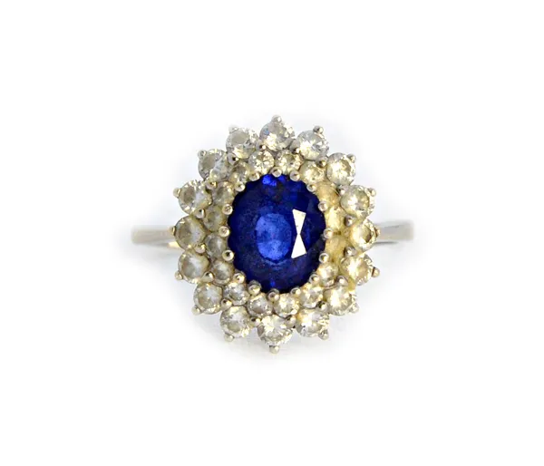 A white gold, sapphire and diamond set oval cluster ring, claw set with the oval cut sapphire at the centre, within a two row stepped surround, of cir