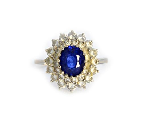 A white gold, sapphire and diamond set oval cluster ring, claw set with the oval cut sapphire at the centre, within a two row stepped surround, of cir