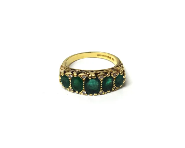 An 18ct gold, emerald and diamond ring, mounted with a row of five oval cut emeralds, graduating in size to the centre stone and with pairs of circula