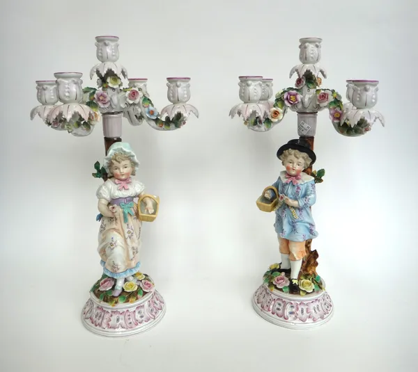 A pair of Sitzendorf porcelain five-light candelabra, late 19th century, modelled as a young boy and girl standing below four scroll arm branches encr
