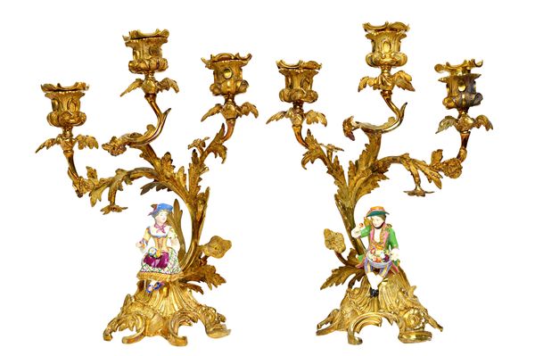 A pair of Minton ormolu mounted three branch candelabra, circa 1830, modelled as a youth and companion, each wearing brightly coloured costume and hol