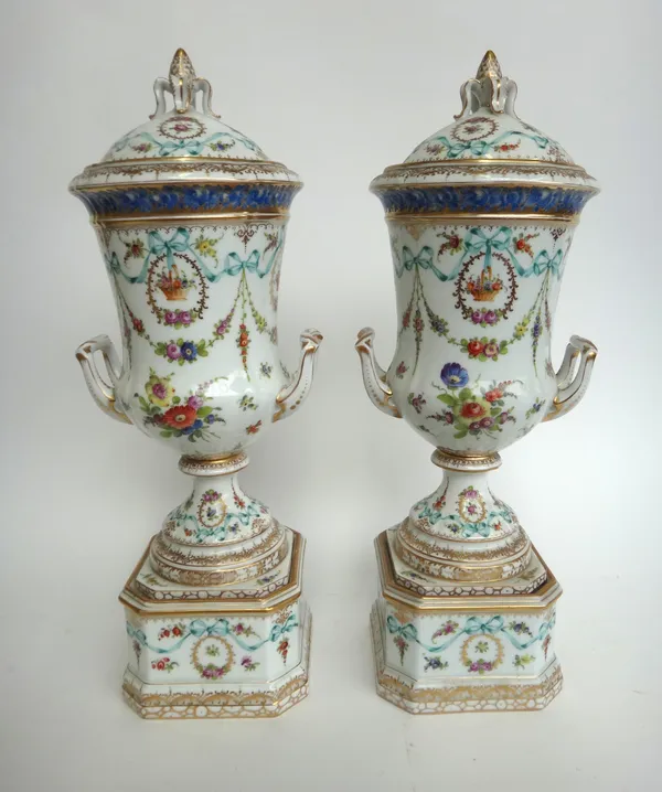 A pair of Dresden porcelain urns and covers, 20th century, each with a gilt foliate finial over a two handled urn, on a canted square base with allove