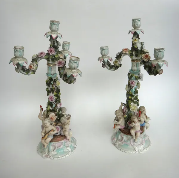 A pair of three branch Sitzendorf porcelain four branch candelabra, early 20th century, each with applied flowers and four musical putti to the shaped
