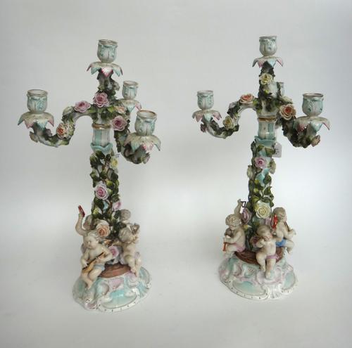 A pair of three branch Sitzendorf porcelain four branch candelabra, early 20th century, each with applied flowers and four musical putti to the shaped