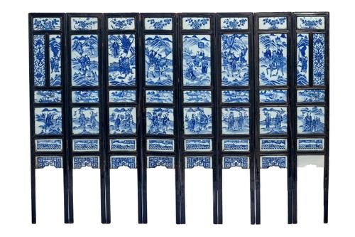 A Chinese blue and white porcelain and ebonised wood eight-fold screen, 19th century, inset with panels of varying size painted with figures in landsc