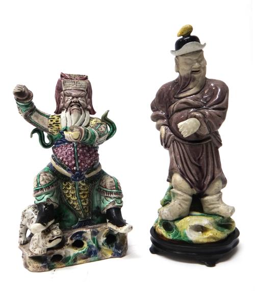 A Chinese biscuit figure of Guandi, 18th/19th century, the god of war seated in armour with one foot resting on the head of a lion dog, (a.f), 22cm. h