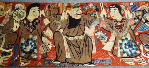 A large Chinese embroidered silk hanging, late 19th/early 20th century, worked with a line of seven performers, 70cm. by 242cm.