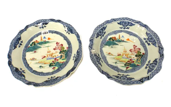 A pair of Chinese famille-rose export dishes, Qianlong, each painted with a central river landscape beneath underglaze-blue floral and diaper pattern