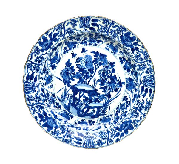 A Chinese blue and white dish, Kangxi, painted in the centre with flowering shrubs and rocks, beneath panelled borders enclosing flowers, 35cm. diamet