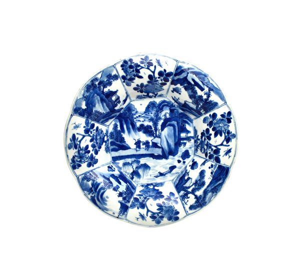 A Chinese blue and white small lobed dish, Kangxi, painted in the centre with figures in a mountainous landscape, beneath a panelled border enclosing