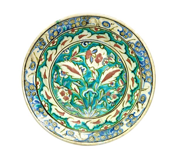 An Iznik pottery dish, 17th century, painted in blue ,turquoise, red and black with a floral spray rising from a tuft of flowers, the cavetto with und