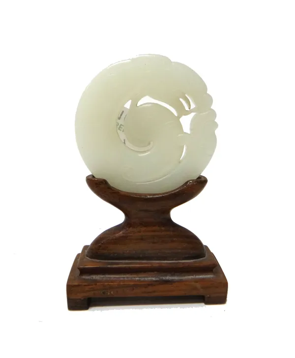 A Chinese white jade plaque, 19th/20th century, carved in the form of a chilong, 6cm. diameter, wood stand. 9