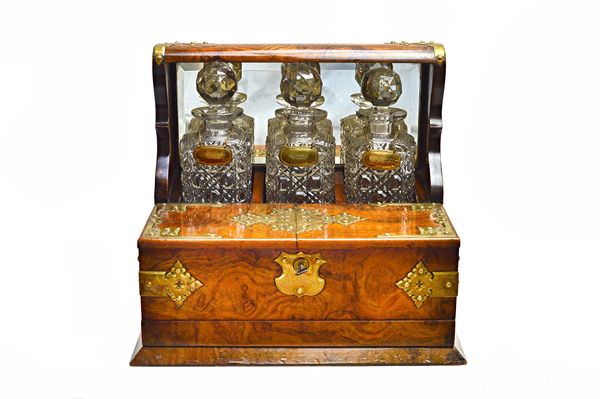 A Victorian brass mounted figured walnut decanter box/games compendium, with a trio of decanters over pair of lift-up tops and fitted lower drawer, en