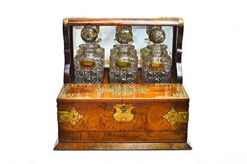 A Victorian brass mounted figured walnut decanter box/games compendium, with a trio of decanters over pair of lift-up tops and fitted lower drawer, en