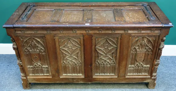A 19th century Gothic Revival oak coffer, the four panel lid over a Gothic tracery four panel front, the corners relief carved with religious figures,