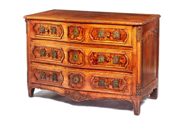 An 18th century French walnut and burr ash serpentine three drawer commode, with shell carved lower frieze, 127cm wide x 85cm high x 68cm deep.  Illus