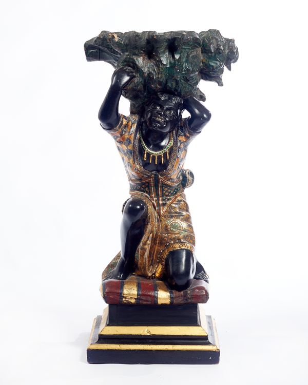 A late 19th century polychrome painted figure of a kneeling Blackamoor, on stepped square base, 42cm wide x 85cm high.  Illustrated