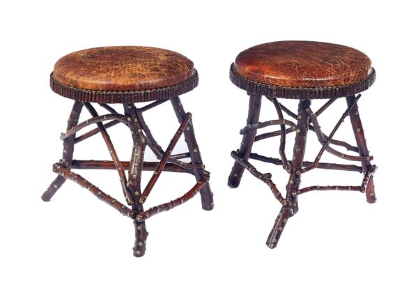 A pair of North European stools, each with leather circular tops raised on naturalistic tree branch supports, with brass floral studded decoration, to