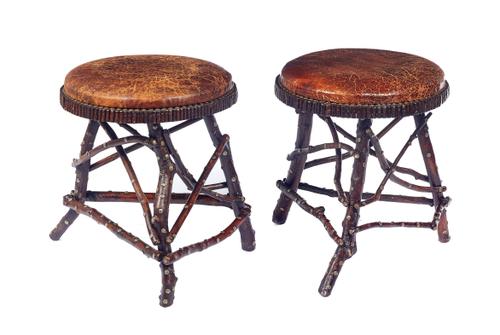 A pair of North European stools, each with leather circular tops raised on naturalistic tree branch supports, with brass floral studded decoration, to