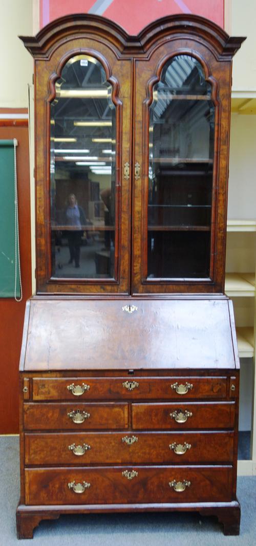 A George II figured walnut bureau bookcase, the double domed top over a pair of bevelled glazed arch top doors, the fall with fitted interior over one