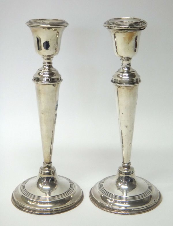 A pair of silver table candlesticks, each of tapering form, raised on a circular base and decorated with reeded bands, height 28cm (loaded), Birmingha