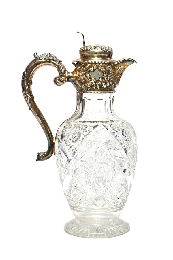 A silver mounted faceted glass hinge lidded claret jug, of vase shaped form, the mount with floral, foliate and scroll embossed decoration within bead