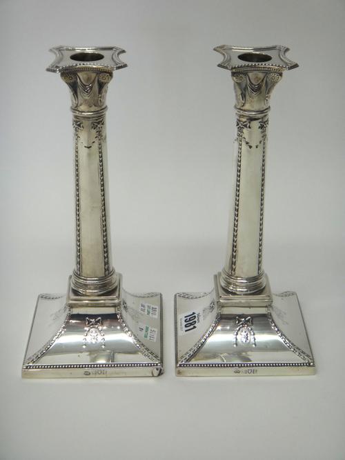 A pair of silver table candlesticks, each designed as a Classical column, raised on a swept square base, loaded, London 1912, height 23.5cm.