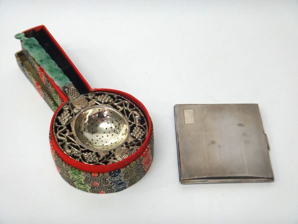 A Chinese tea strainer, the border pierced and embossed with leaves, berries and animals and with a carved jade handle, with the original box and a si