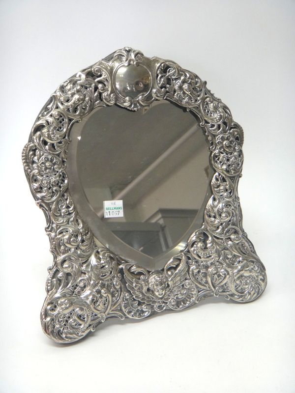 A late Victorian silver mounted heart shaped strut backed mirror, the front with a cherub's face motif, otherwise with scroll pierced and embossed dec