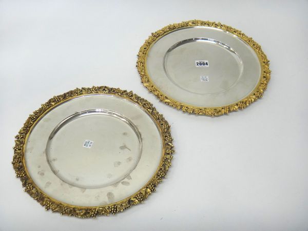 A pair of silver and gilt shallow dishes, each of shaped circular form, decorated with a cast and pierced gilt border of fruiting vine, by C.J. Vander