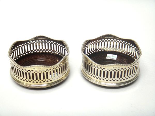 A pair of silver bottle coasters, each with pierced decoration within a wavy gadrooned rim and having a turned wooden base, with a silver disc to the