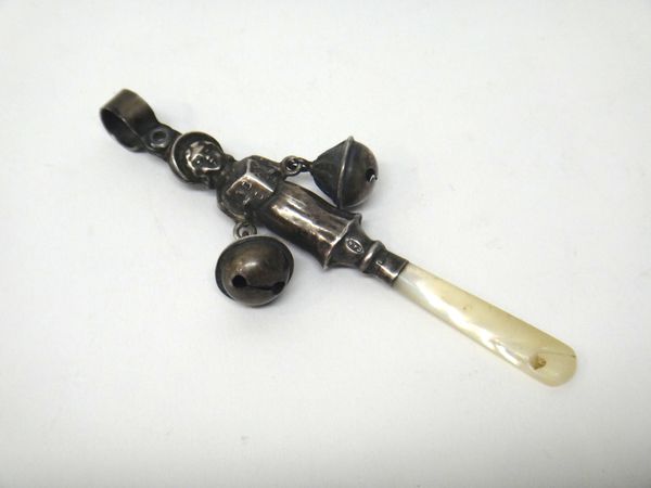 A silver and mother of pearl baby's rattle, designed as the standing figure of a girl holding an alphabet book, fitted with two bells, a suspension lo