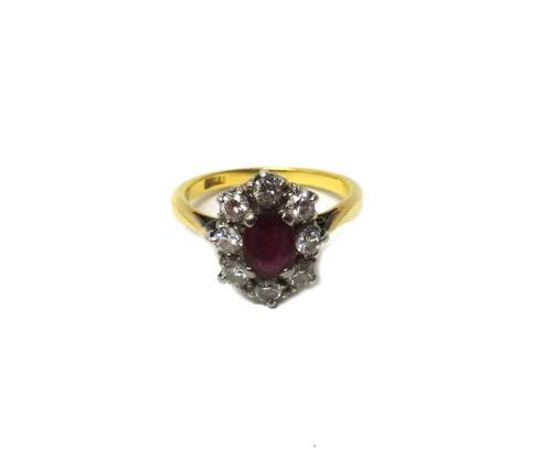 A gold, ruby and diamond set nine stone oval cluster ring, claw set with the oval cut ruby at the centre, in a surround of eight circular cut diamonds