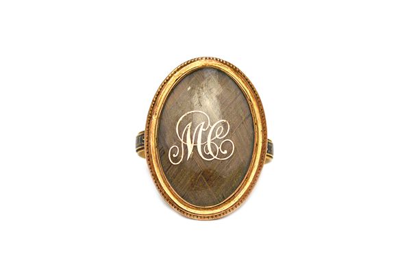 A George III gold and black enamelled mourning ring, the oval bezel glazed with a woven hair locket compartment and with the gilt script initials 'M C