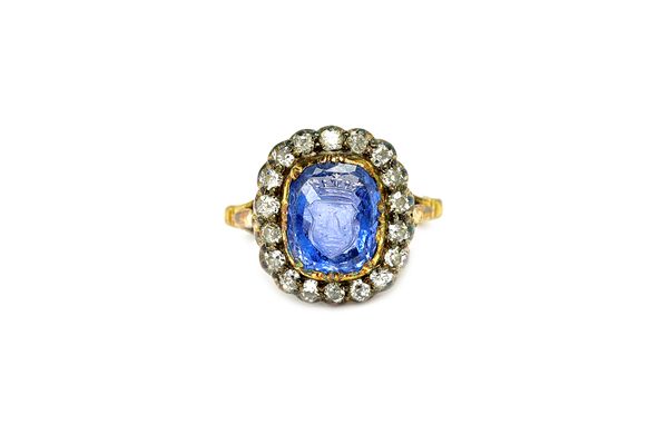 A diamond and sapphire intaglio cluster ring, mounted with the cushion shaped sapphire intaglio to the centre, carved as the Swedish Uggla crest with