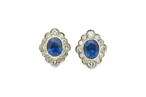 A pair of sapphire and diamond oval cluster ear studs, each collet set with the oval cut sapphire at the centre, within a surround of circular cut dia