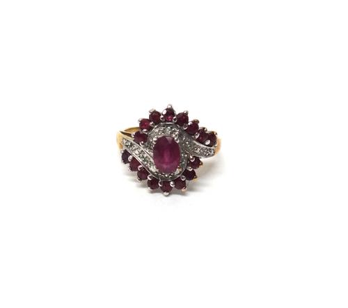 A 9ct gold, ruby and diamond ring, in a spiral cluster design, claw set with the principal oval cut ruby at the centre and with rows of eight circular