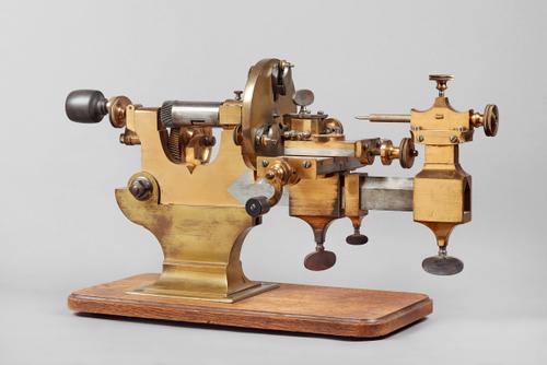 A Swiss steel and brass watchmaker's mandrelSecond half 19th centuryWith square brass foot, steel bed, adjustable tool bed, helical gearing, on an oak