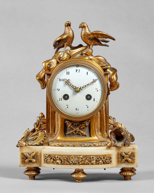 A French ormolu and white marble mantel clockIn the Louis XVI style, circa 1900The fluted arched case surmounted by a pair of doves on a flaming torch