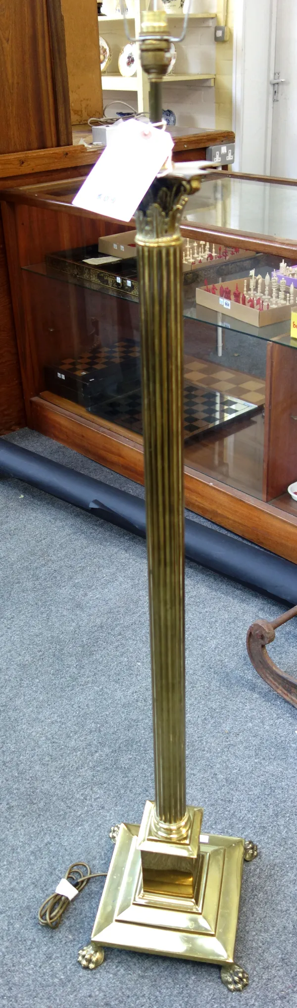 A brass standard lamp formed as a reeded Corinthian column, on a square stepped base with paw feet, 123cm high excluding fitments.