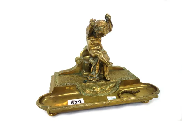 A French gilt metal pen tray, circa 1880, of rectangular form, surmounted by a boy in the manner of Boucher, seated on a chair with fluted volutes to